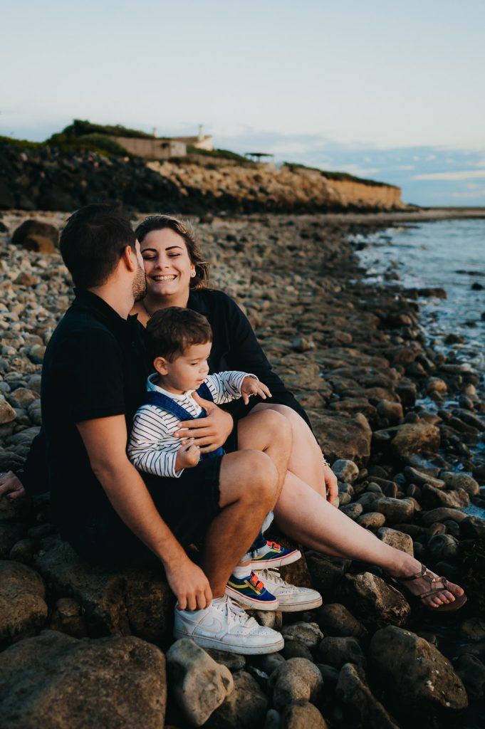 Une famille de 3 est assise sur la plage au bord du bassin, la femme sourit et est joyeuse. Un moment de vie capté par L'instant par Phé, Photographe Gironde & Bordeaux.