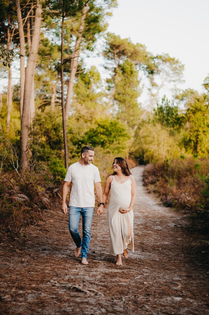 Un couple se tient la main et se promène en forêt. Un moment de vie quotidienne capturé par l'Instant par Phé, Photographe Gironde & Bordeaux, pendant leur séance photo grossesse.