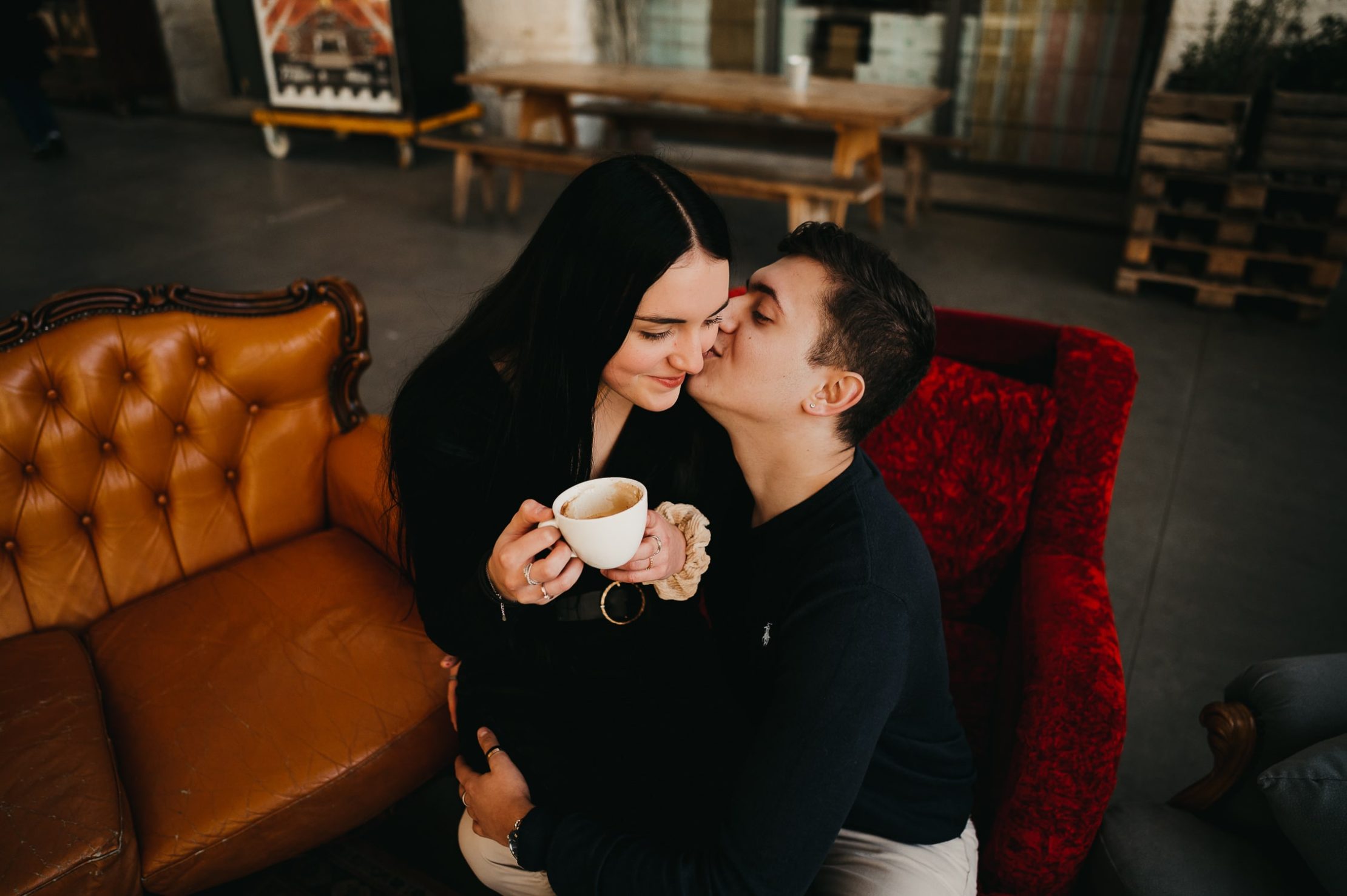 un jeune couple qui se font un bisous tout en prenant une tasse de café lors d'une séance couple sur Bordeaux