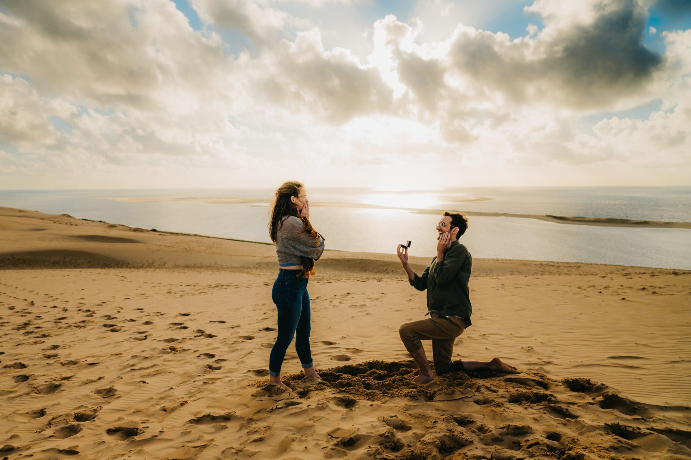 une jeune femme surprise, face à elle, son petit ami genou à terre qui la demande en mariage