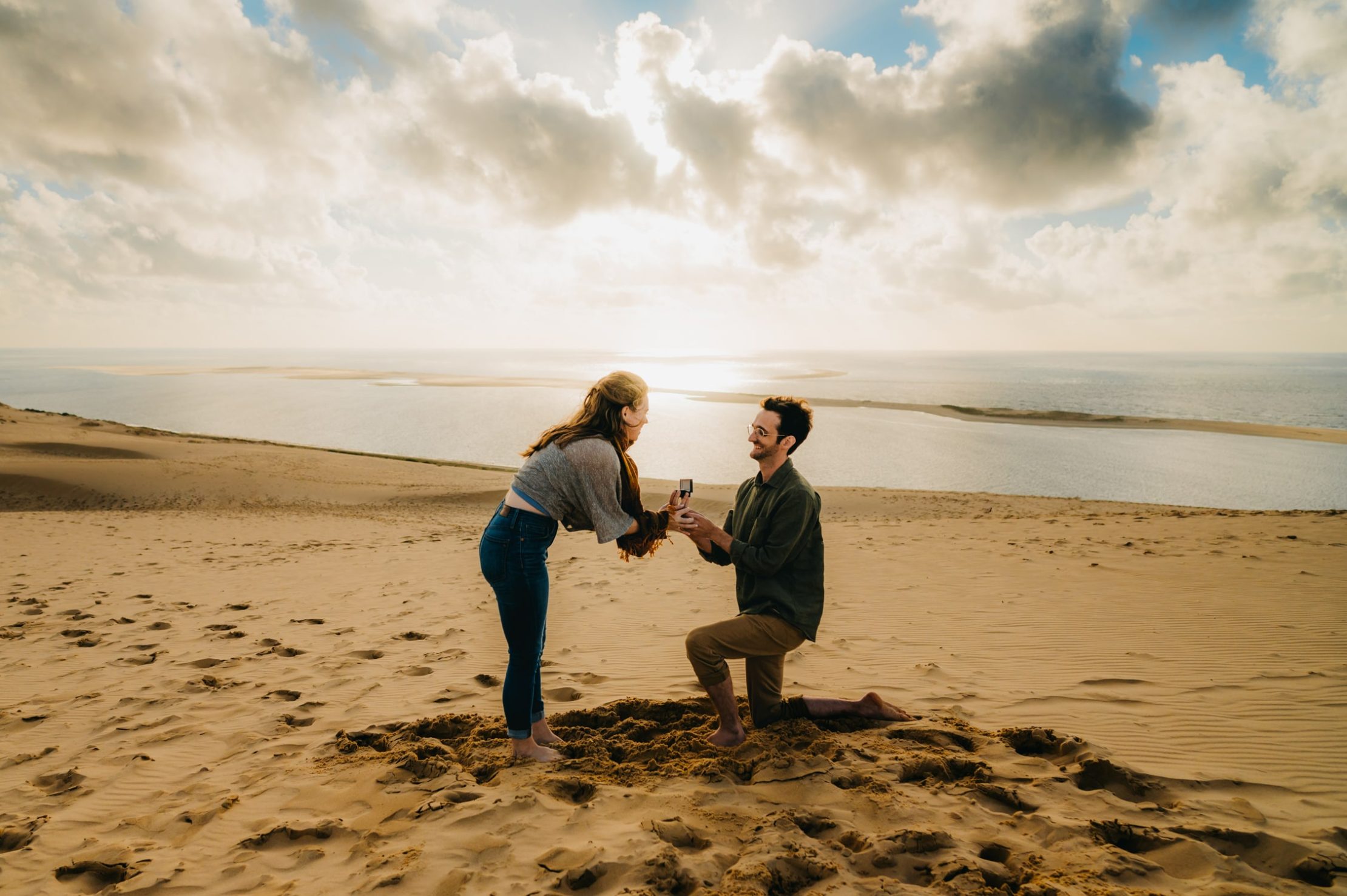 Une photographe couple à Arcachon qui fige un moment entre un jeune couple, en haut de la dune du pyla. Le jeune homme, un genou sur le sable demande sa petite amie en mariage