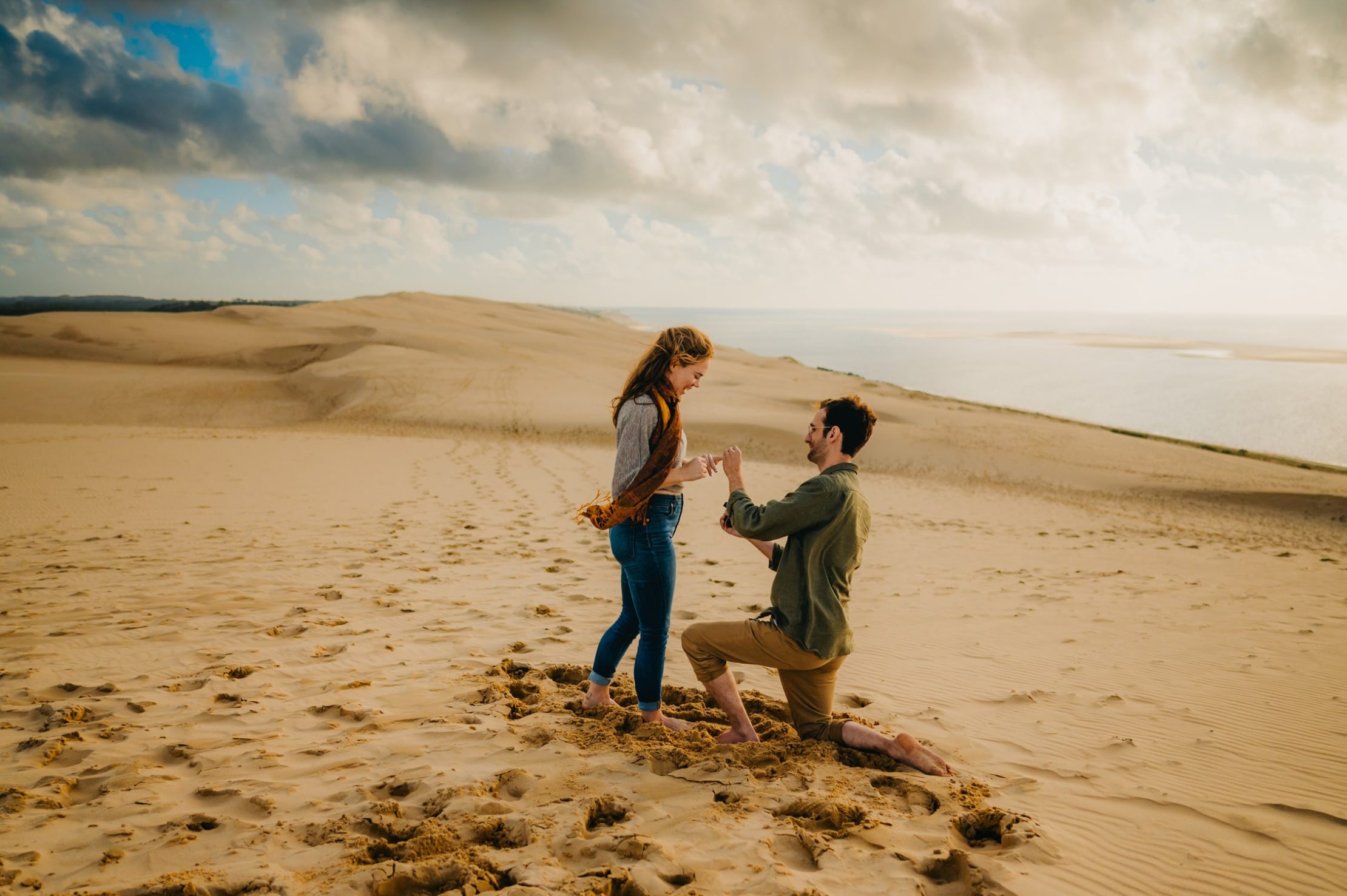 Une photographe couple à Arcachon qui fige un moment entre un jeune homme vient de demander sa petite copine en fiançailles, il lui met la bague au doigt, face à la mer, sur le sable de la dune du pilat
