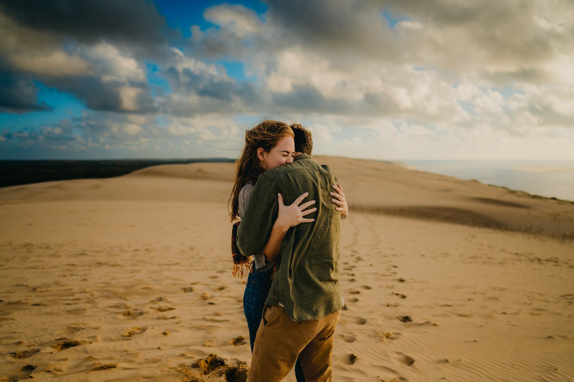 Une photographe couple à Arcachon qui fige un moment d'un jeune couple d'amoureux blotti l'un contre l'autre sur le sable de la dune du pilat