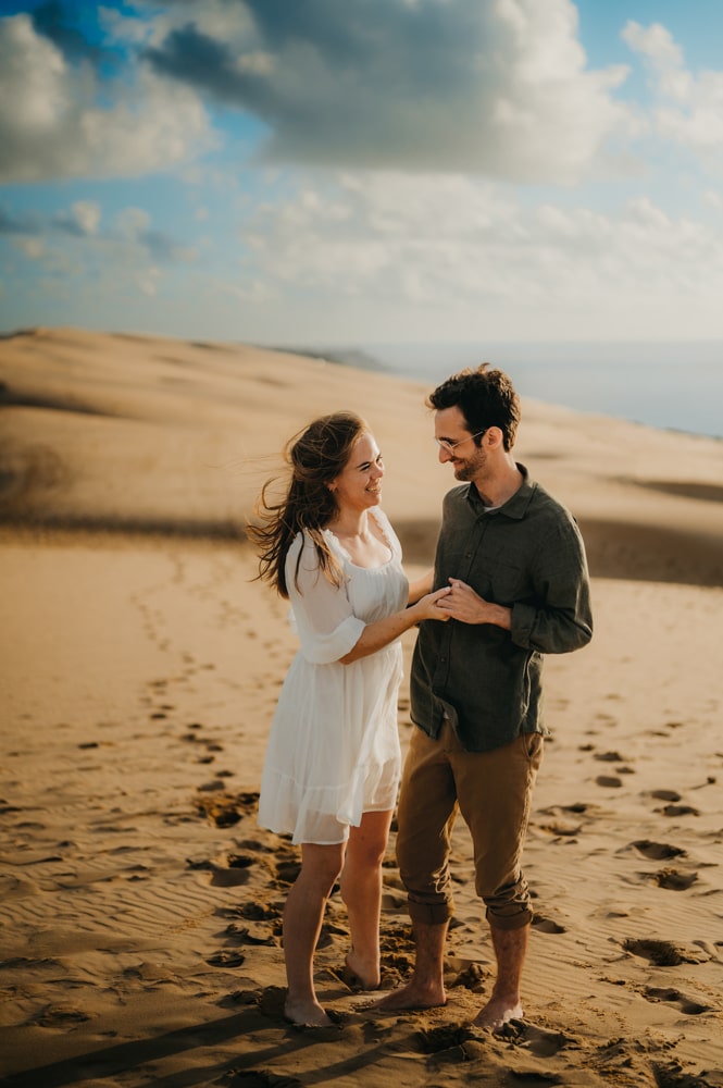 Couple de jeunes amoureux qui se tiennent les mains face à face sur le sable, à la dune du pyla