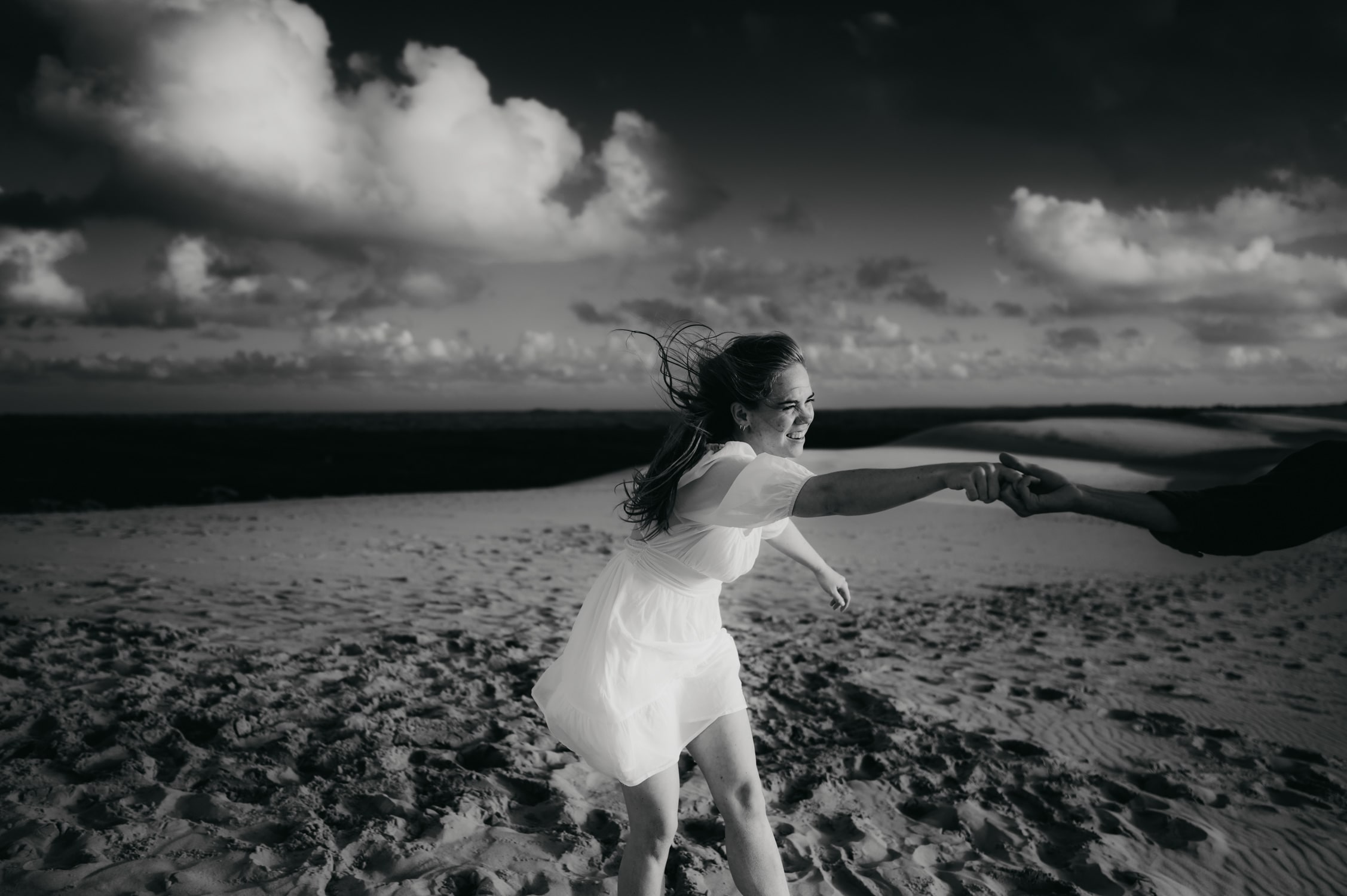 Jeune femme qui joue avec son petit copain sur le sable, à la dune du pilat, cheveux dans le vent