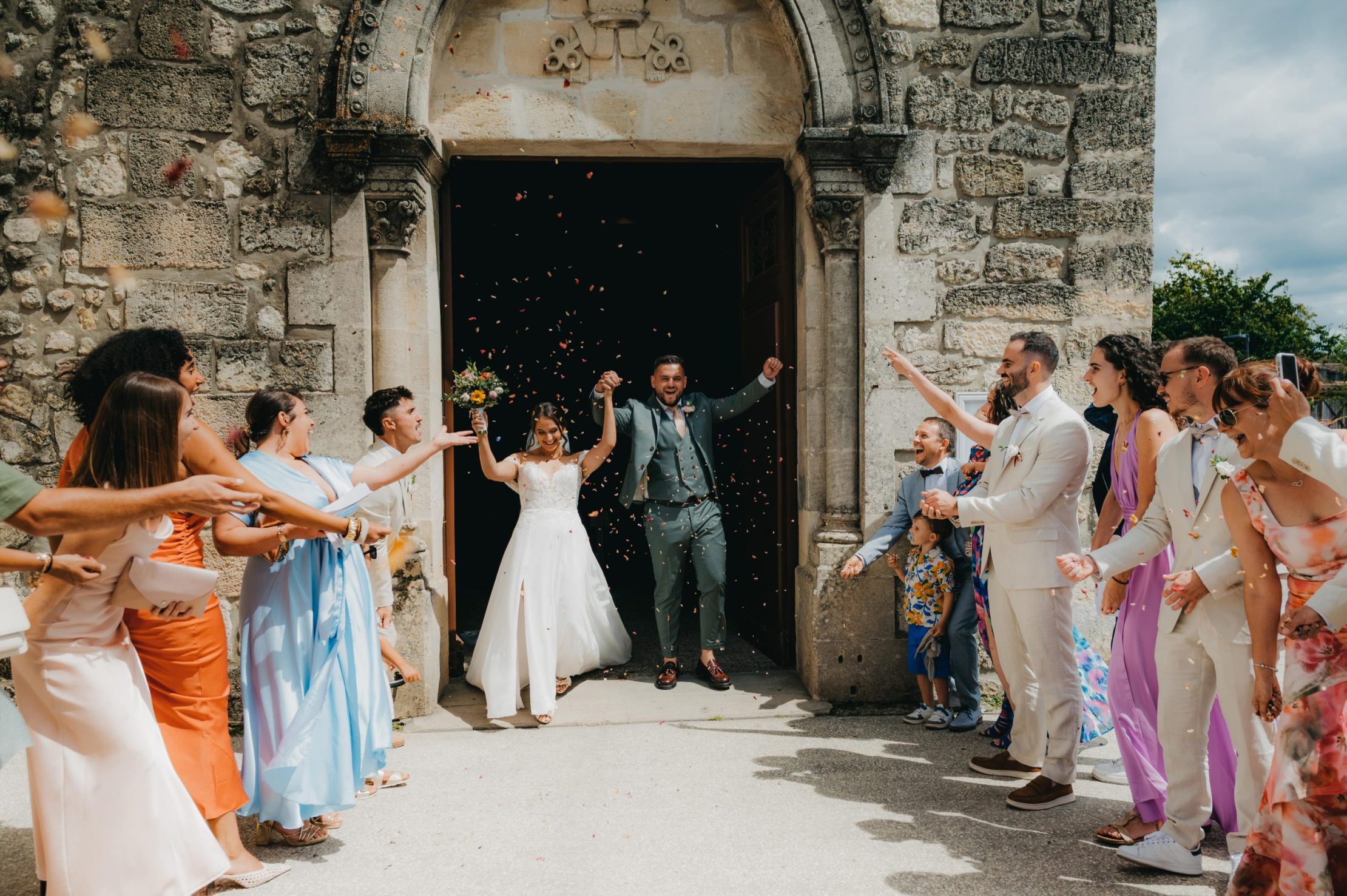 les mariés qui vivent à fond leur sortie d'église et les invités qui applaudissent