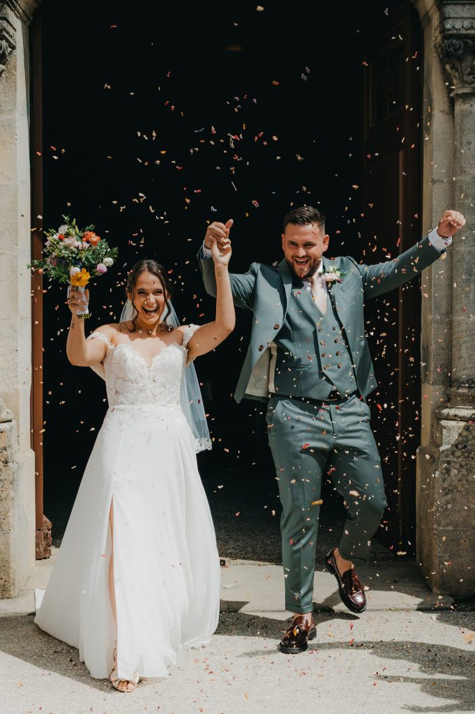 portrait des mariés à la sortie d'église sous une pluie de confettis