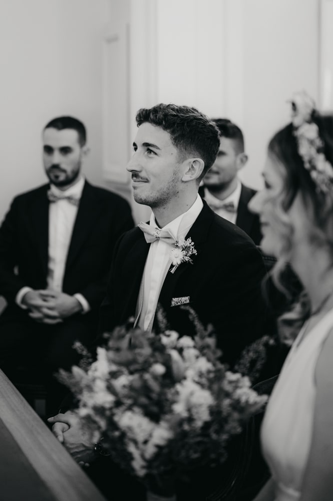 un marié, assis et qui écoute le maire réciter les textes de lois lors d'une cérémonie civile