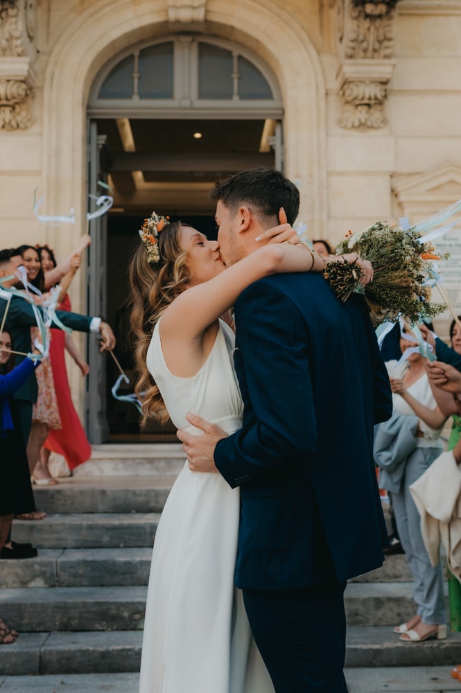 un bisou fougueux d'un jeune couple de mariés devant une mairie