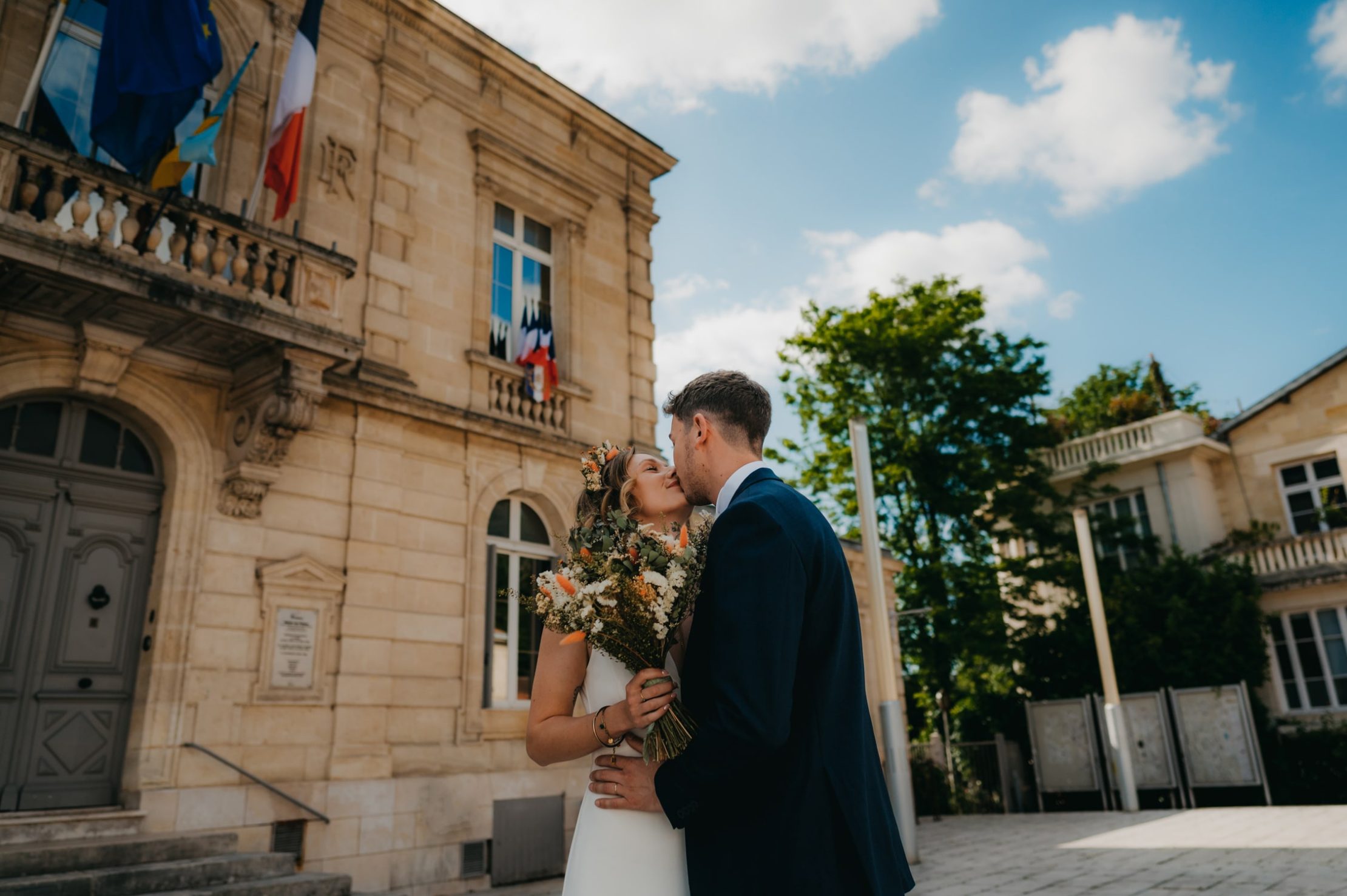 deux mariés qui s'embrassent après leur cérémonie civile devant la mairie