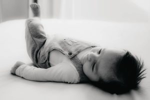 Le bébé est allongé sur le dos et balance sa jambe en l'air. Un moment capté par L'instant par Phé, photographe bébé Bordeaux et Gironde.