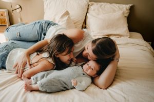 La maman, la grande soeur et le bébé sont allongées sur le lit pendant la séance photo bébé à Bordeaux.