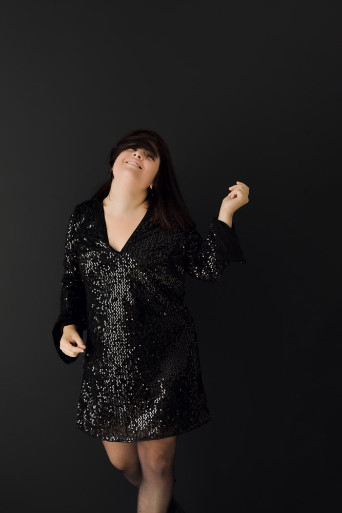 La photographe bordeaux & gironde danse en robe de soirée à paillettes noire sur fond noir.