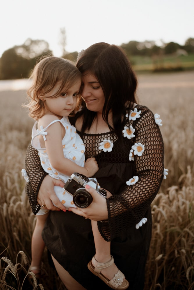 La photographe bordeaux & gironde porte sa fille dans ses bras pendant une séance photo dans un champ de blé.