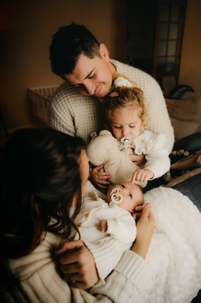Une famille de 4 fait la séance photo naissance à la maison. Ils sont chez eux, assis dans le salon, et se font des calins. Beaucoup de douceur captée par L'instant par Phé, photographe bébé Bordeaux et Gironde.