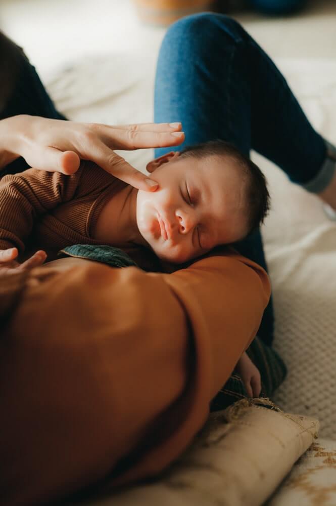 Un bébé dort dans les bras de sa maman. Sa maman lui caresse le visage. Un moment de douceur photographié par L'instant par Phé, photographe bébé Bordeaux et Gironde.