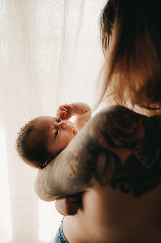 La maman fait du peau à peau avec son bébé qui la regarde dans les yeux. Un moment de partage et de douceur pendant une séance photo bébé à Bordeaux en Gironde.