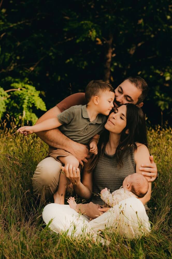 Une famille de 4 est assise dans l'herbe. Ils se font des bisous. Un moment photographié par L'instant par Phé, photographe bébé Bordeaux et Gironde.