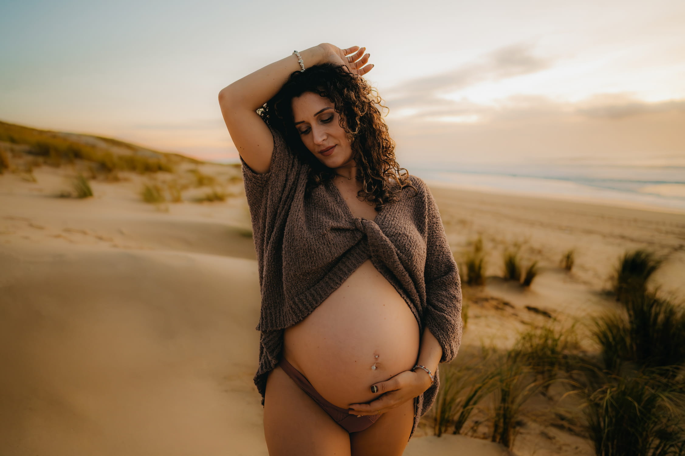 Femme enceinte souriante dans les dunes au coucher du soleil