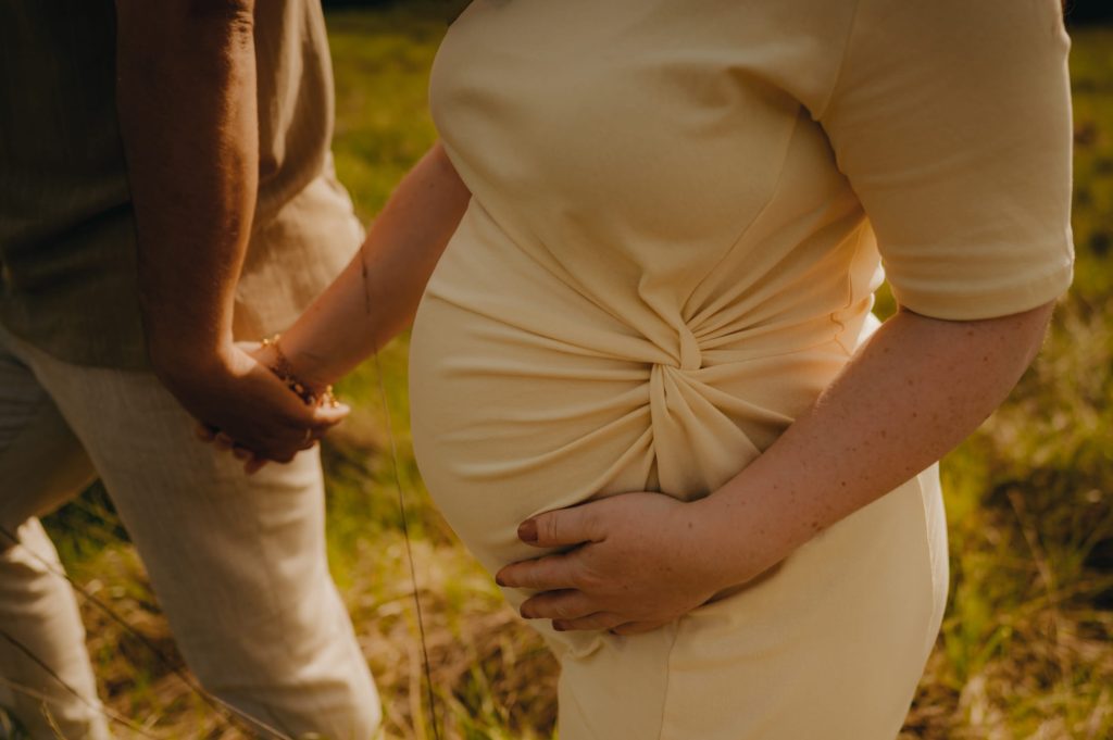 Détail des mains des futurs parents sur le ventre rond pendant une séance grossesse dans l’Entre-deux-Mers