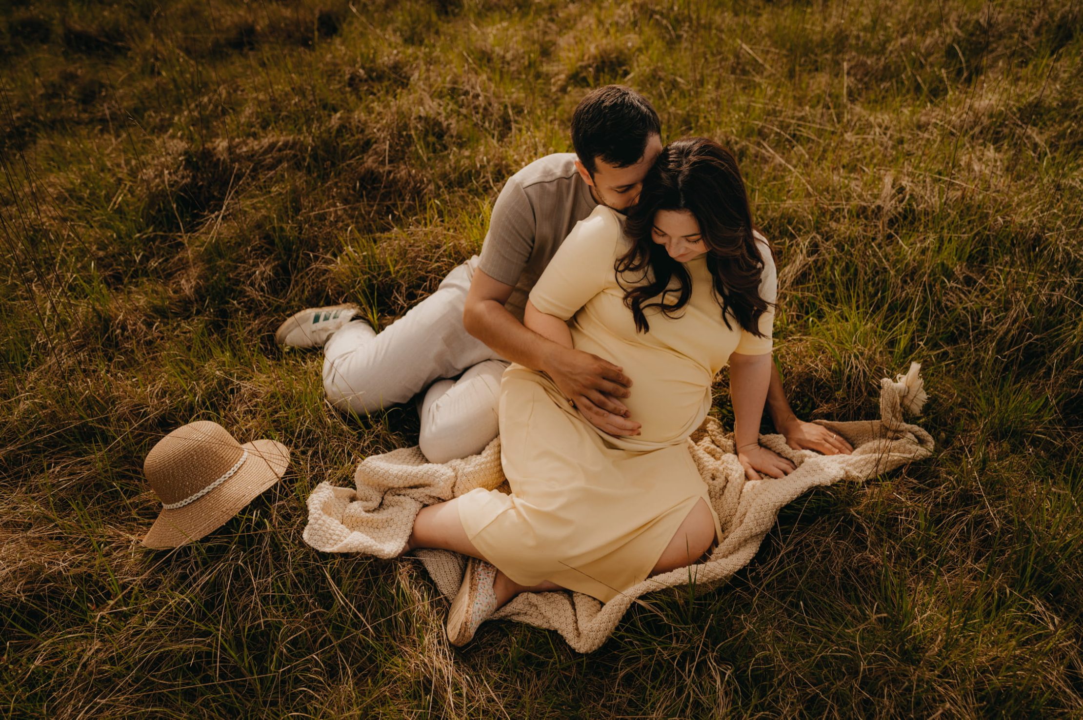 Future maman allongée dans l’herbe pendant sa séance photo grossesse naturelle